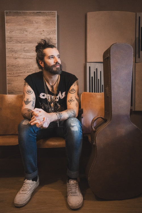 Waxx, assis sur un siège, à côté de son étui de guitare