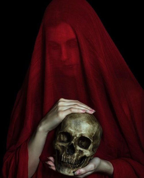Photographie d'une femme drapée d'un voile rouge avec une tête de mort dans les mains